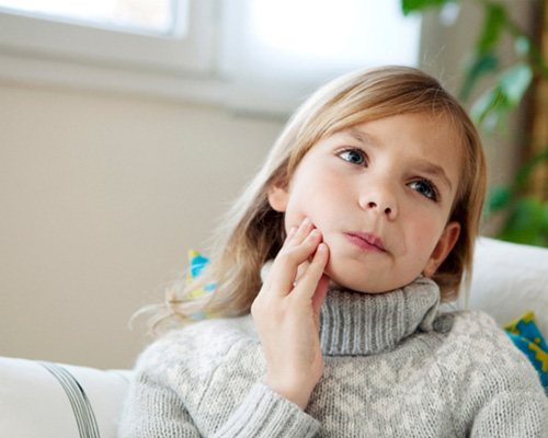 Child holding cheek due to tooth pain at home