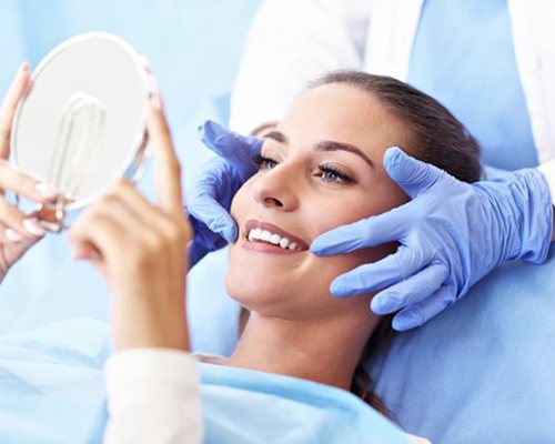 woman in dental chair admiring her smile in hand mirror