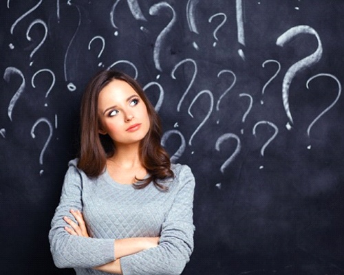 confused young woman in front of chalkboard covered in question marks