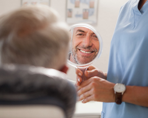 Man smiling in mirror while visiting Bedford emergency dentist