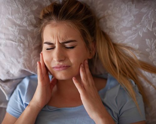 a woman holding her cheek due to jaw pain