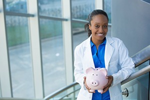 smiling dentist holding a pink piggy bank 