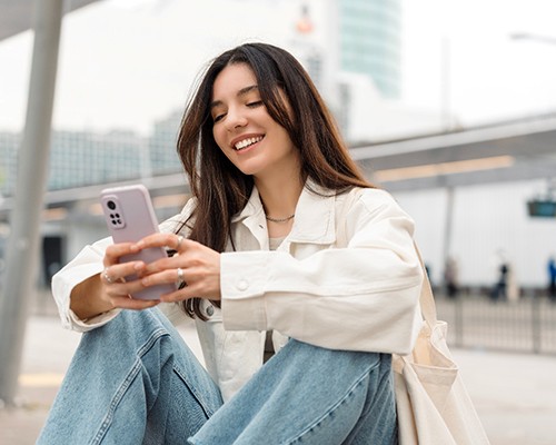 Teen girl smiling while looking at phone outside