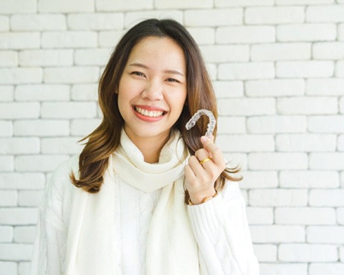 smiling woman holding Invisalign in Bedford