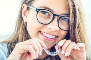Woman smiling and holding Invisalign in Bedford