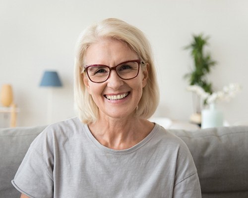 Woman in glasses smiling after full mouth reconstruction in Bedford, TX