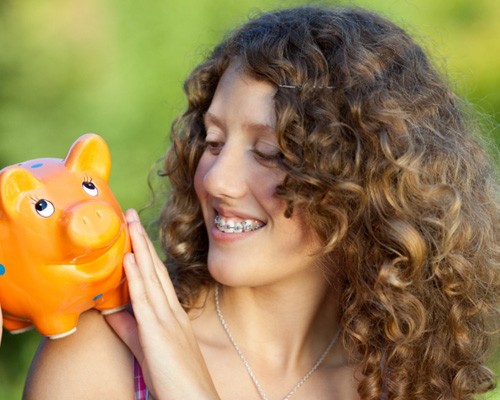 Someone with braces looking at a piggy bank